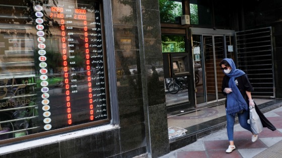 An Iranian woman wears a protective face mask as she walks next to an electronic currency board in Tehran