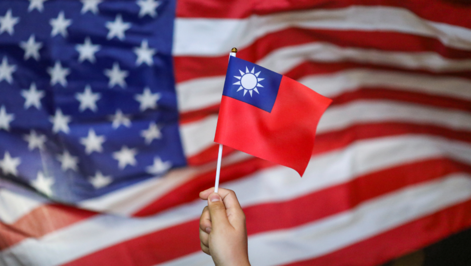 An anti-government protester holds a Taiwan national flag as an U.S. flag flutters in the background