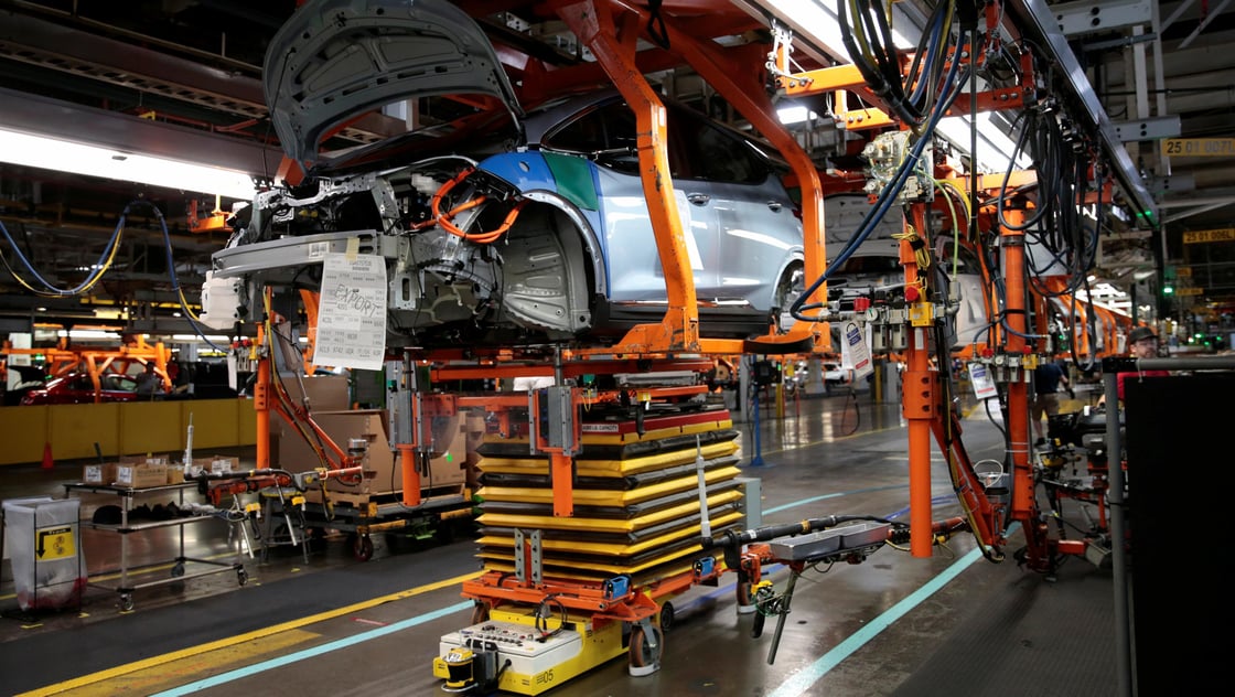 An automated guided vehicle carrying a battery pack moves under a partially assembled 2018 Chevrolet Bolt EV vehicle on the assembly line at General Motors Orion Assembly in Lake Orion, Michigan