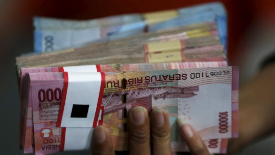 An employee of a money changer holds a stack of Indonesia rupiah notes