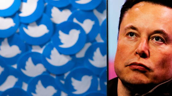 An image of Elon Musk is seen on a smartphone placed on printed Twitter logos