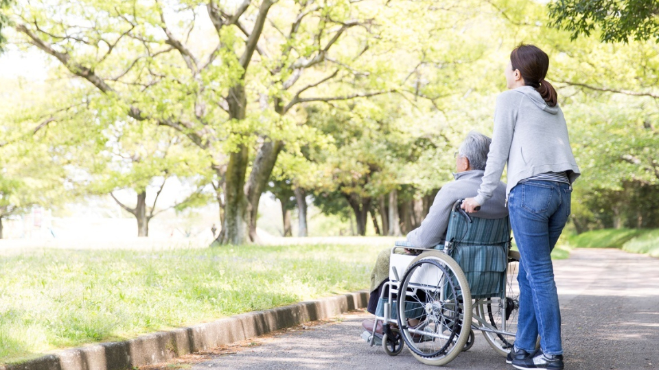 An elderly man in wheelchair and care helper. 