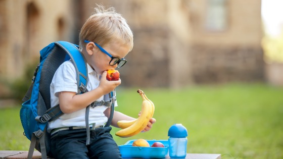 Boy eating fruit with backpack on