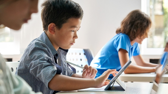 Boy in class uses tablet at desk