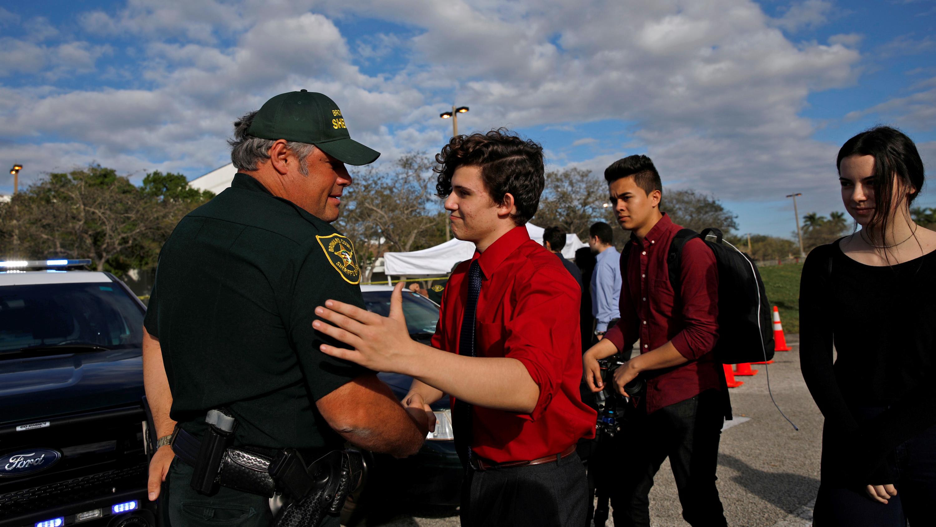 Alfonso Calderon, a student who was at Marjory Stoneman Douglas High School during the mass shooting, greets the police officer Brad Griesinger in front of the school.
