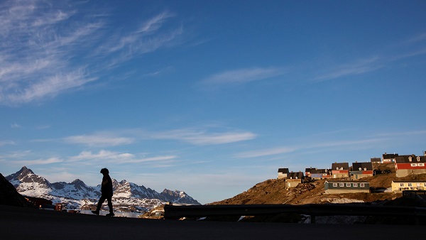 A man walks along the road in the evening sunshine through the town of Tasiilaq, Greenland.
