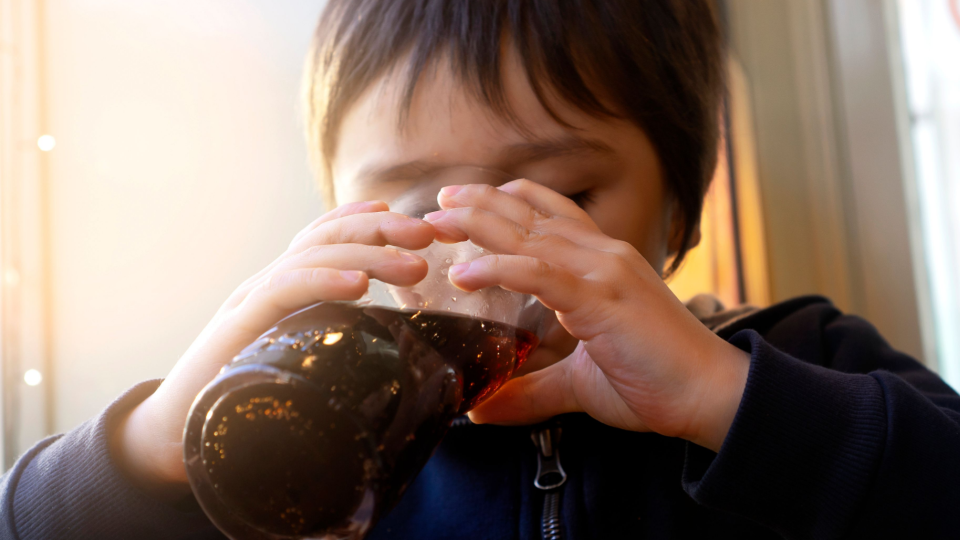 Child drinking soda from a glass.