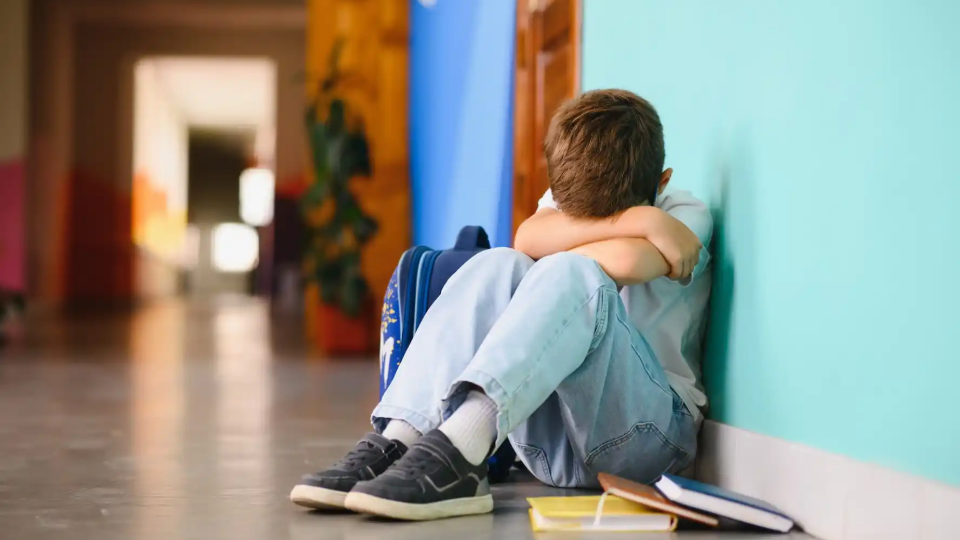 Child sitting in a school hallway with head in his arms