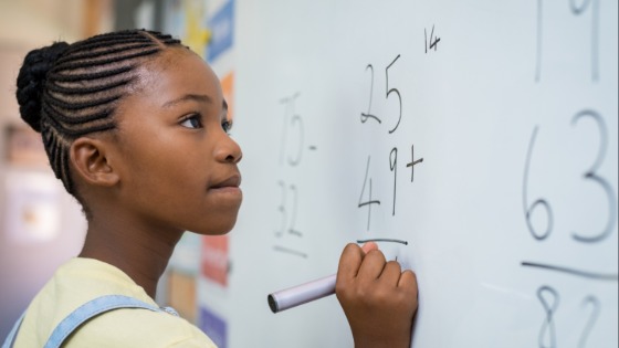 Child solving math equation on whiteboard