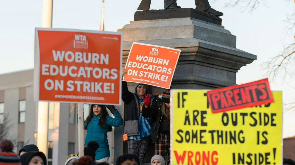 Children support their teachers and parents on strike by holding signs on a Civil War monument during a rally in Woburn