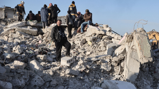 Civilians and White Helmets members inspect a building that collapsed in the city of Harem following the devastating earthquake that struck the Turkish-Syrian border