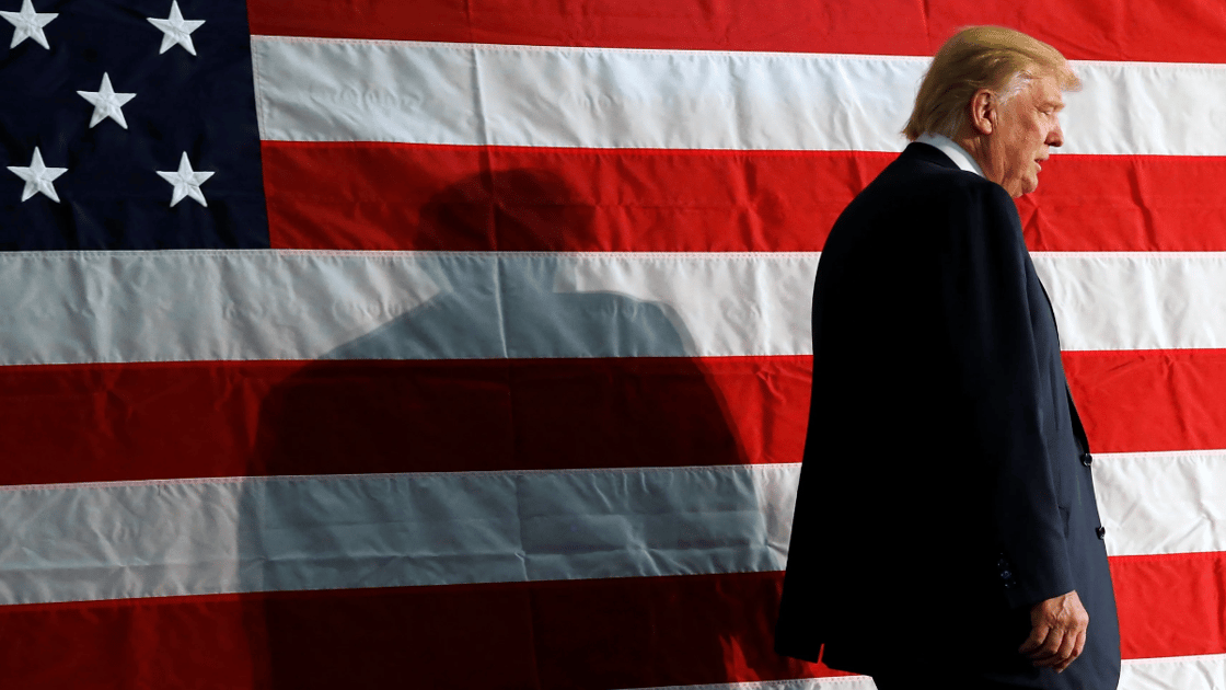 Donald Trump stands in front of large American flag