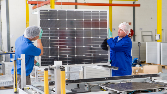 Factory workers lifting new solar panel from production line