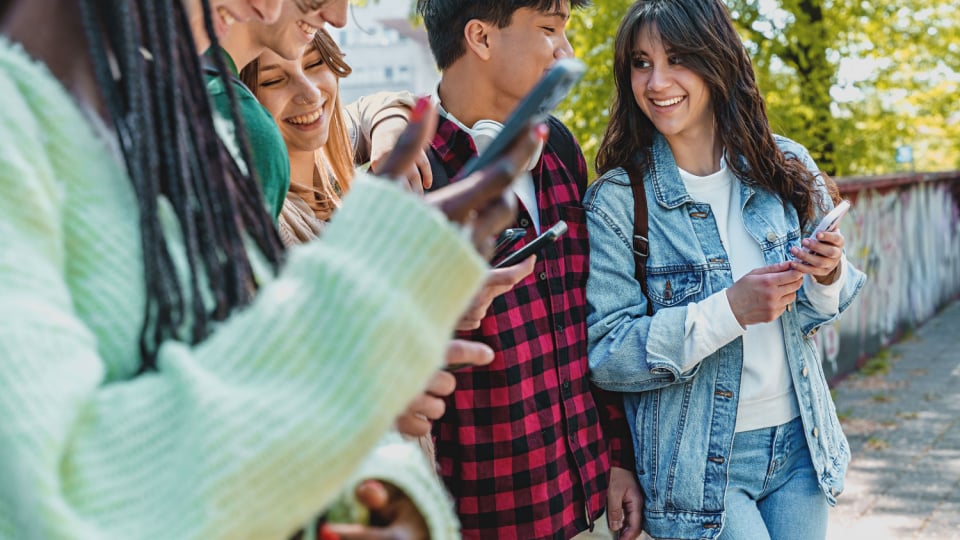 Gen Z students in a park, joking and checking social networks on phones