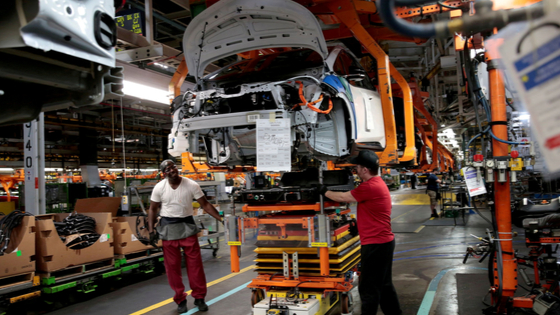 General Motors assembly workers connect a battery pack underneath a partially assembled 2018 Chevrolet Bolt EV