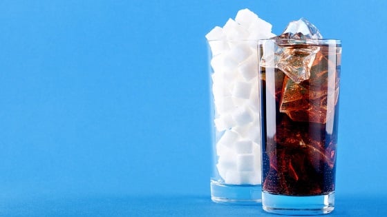 Glass of soda next to a glass full of sugar cubes