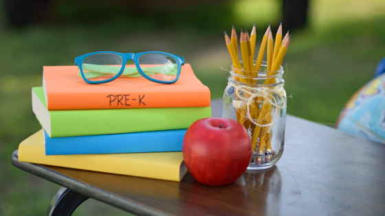 Glasses, books, pencils, and apple sitting on table