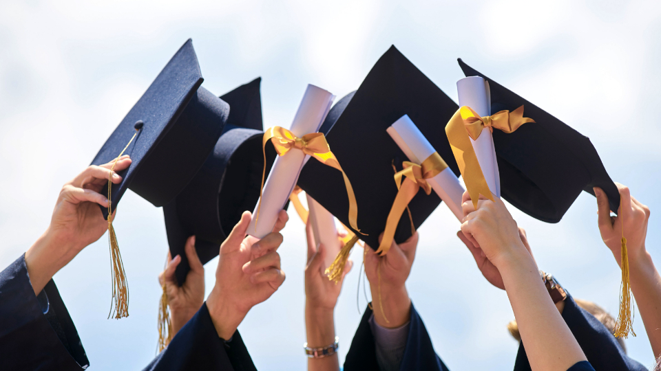 High school graduates raise their caps and diplomas at ceremony.