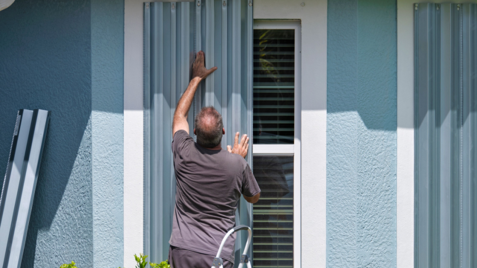 Home owner boarding up windows with steel storm shutters for hurricane protection of residential house. Protective measures before natural disaster in Florida. North Port, USA 