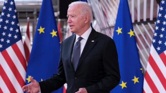 Joe Biden stands in front of U.S. and EU flags.