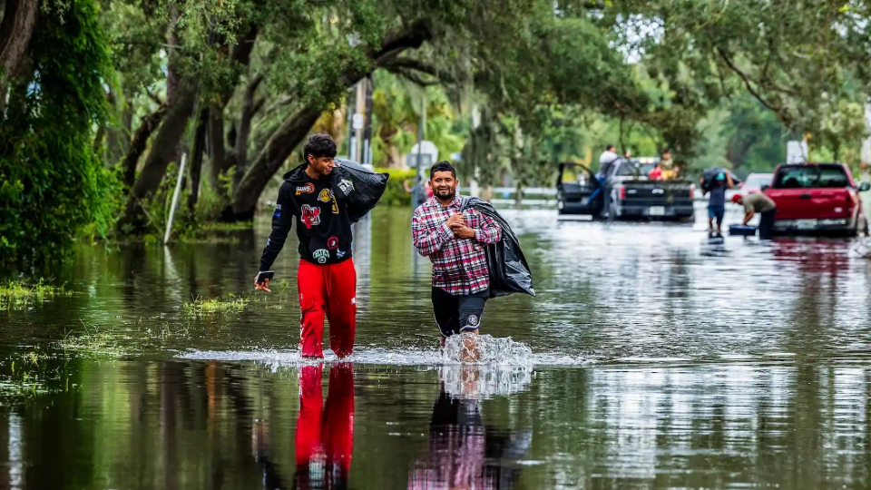 Juan Jose Muñoz, left, and Elvin Antonio Urbina walk with their belongings through a flooded street in North Tampa, Florida