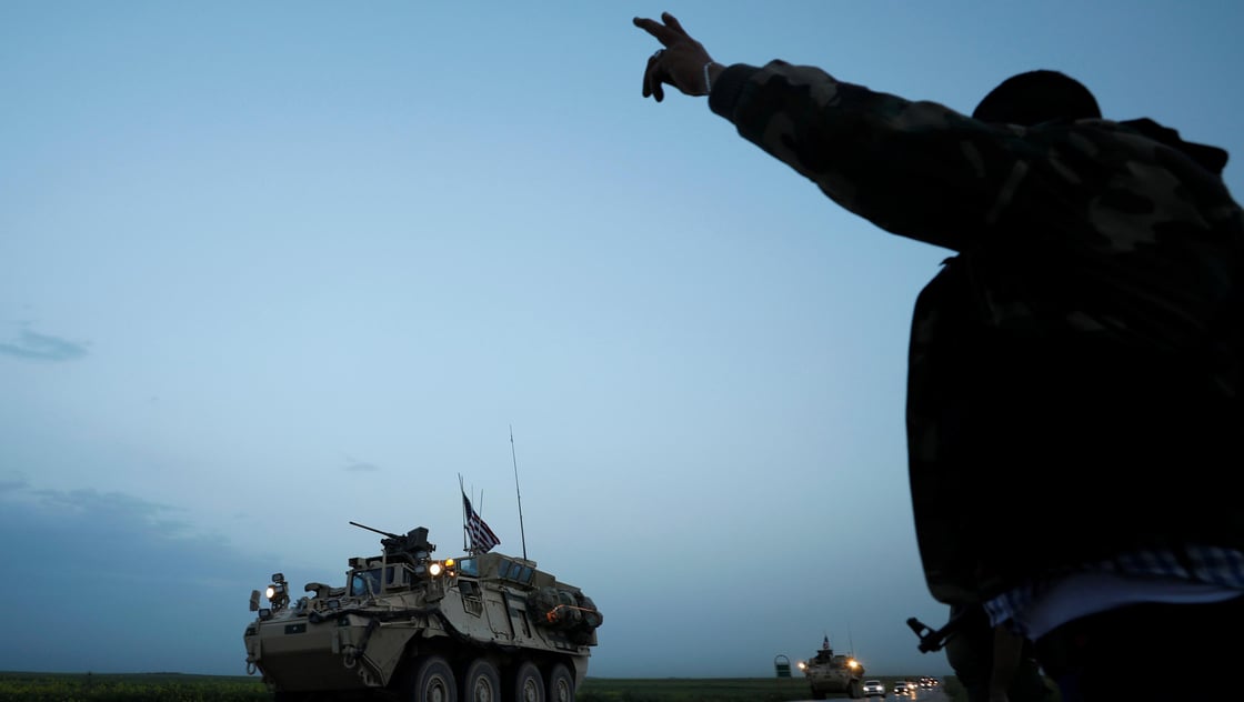 Kurdish fighter from the Peoples Protection Units (YPG) gestures at a convoy of U.S military vehicles driving in the town of Darbasiya next to the Turkish border