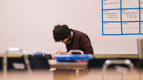 Male student working at desk in front of a whiteboard in a classroom