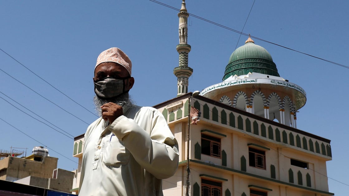 Man in mask walking past mosque in Pakistan