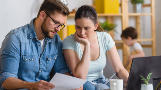 Mother and father discuss bills with child in background.