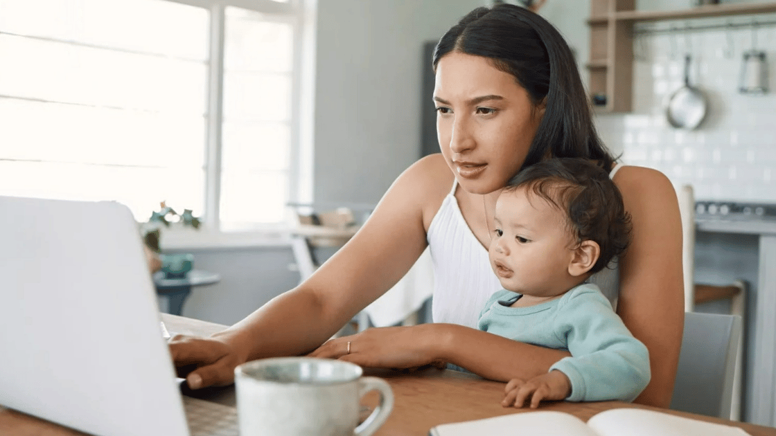 Mother works on laptop with baby in her lap