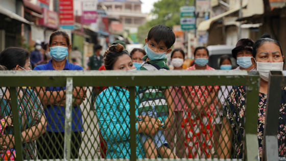 Oum Sreykhouch carries her child as she stands with her neighbours behind a lockdown barrier to ask for food donations