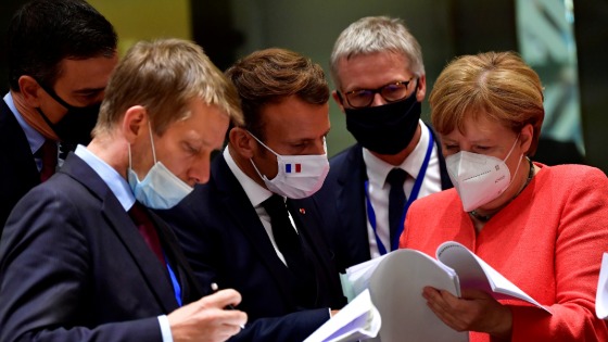 Pedro Sanchez, Emmanuel Macron, and Angela Merkel look over documents at an EU summit