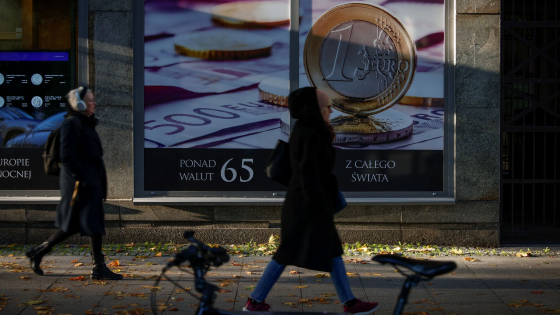 People are seen walking past a shop for buying and selling gold and silver with a Euro coin printed on the shop window in Warsaw