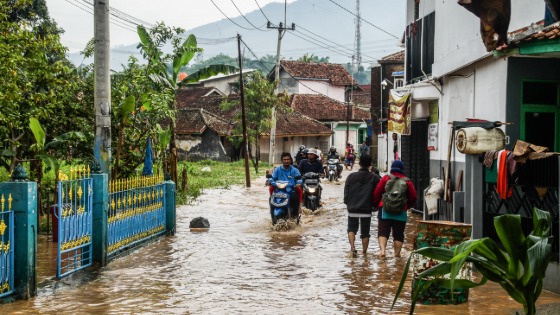 People ride motorcycles through a flooded road in Cihanjuang Village