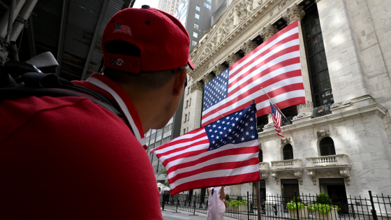 People walk past the facade of the New York Stock Exchange draped in a large American Flag