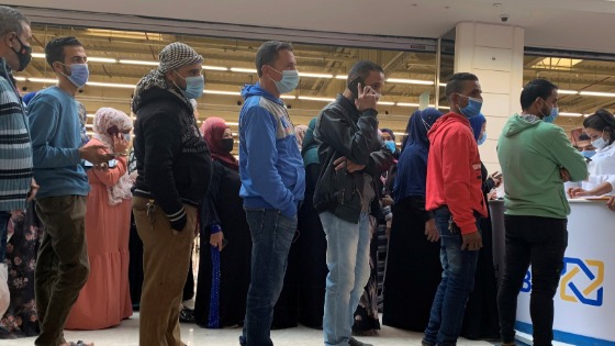 People wearing protective face masks wait in line in front of Al Ahli Bank of Kuwait