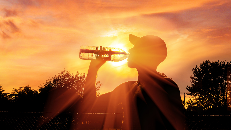 Person drinking water from bottle as sun sets behind them