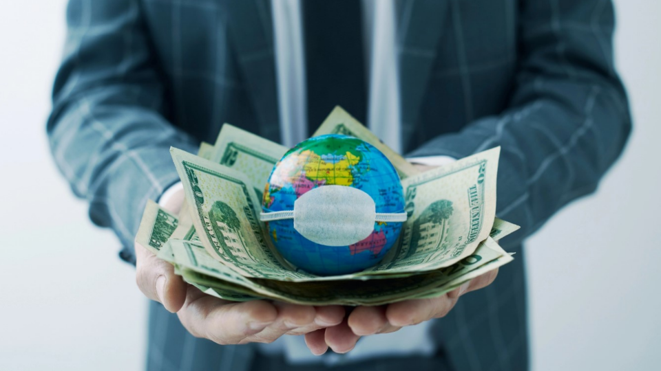 Person holding money and globe with surgical mask