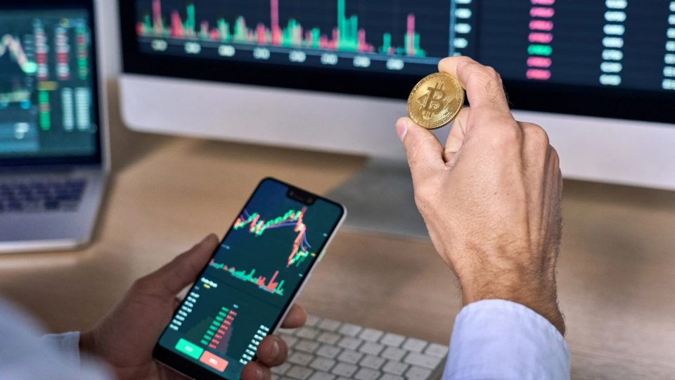 Person holding physical representation of Bitcoin while holding phone in other hand