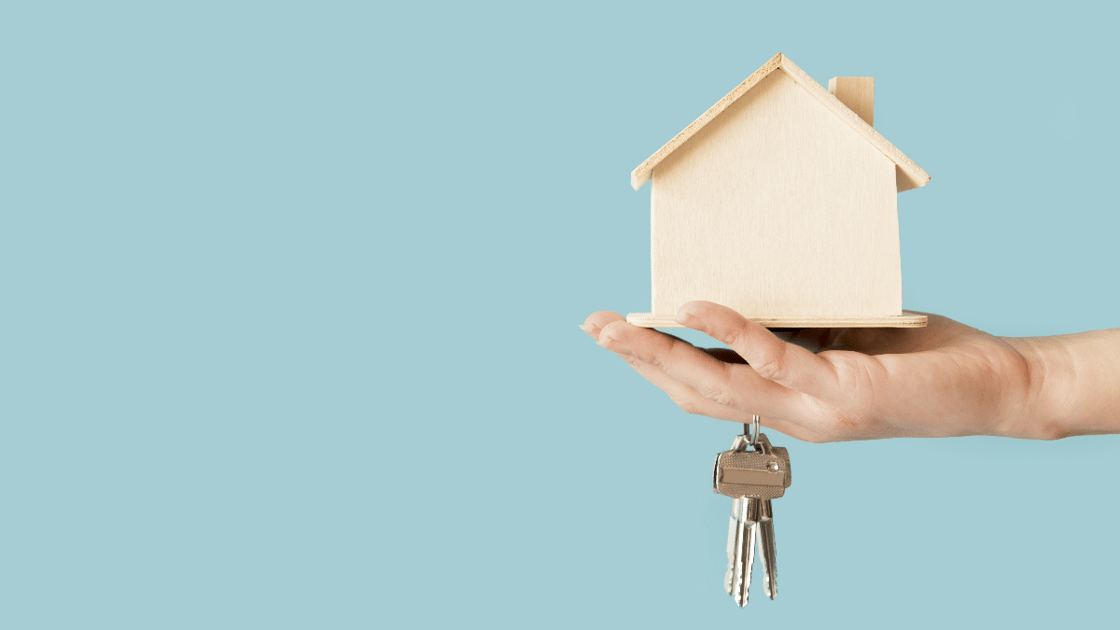 Person holding wooden house model and keys