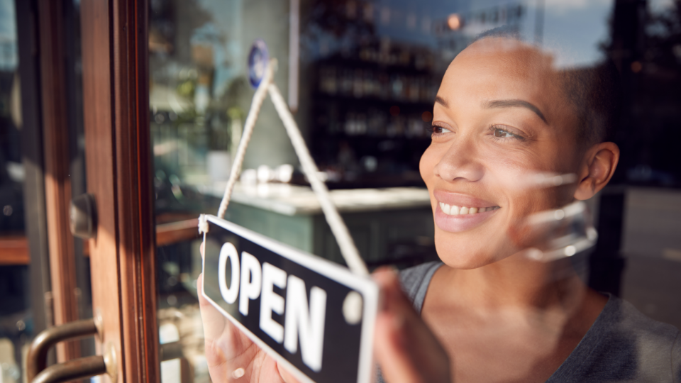 Person looking out of a window with an open sign for their business