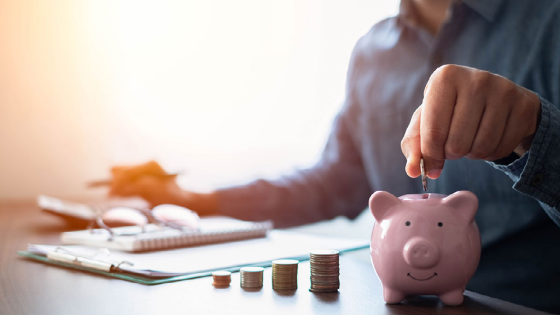 Person sitting at a desk putting a coin into a piggy bank