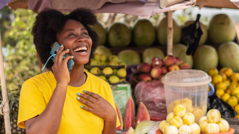 Person talking on the phone and smiling in front of fruit stall