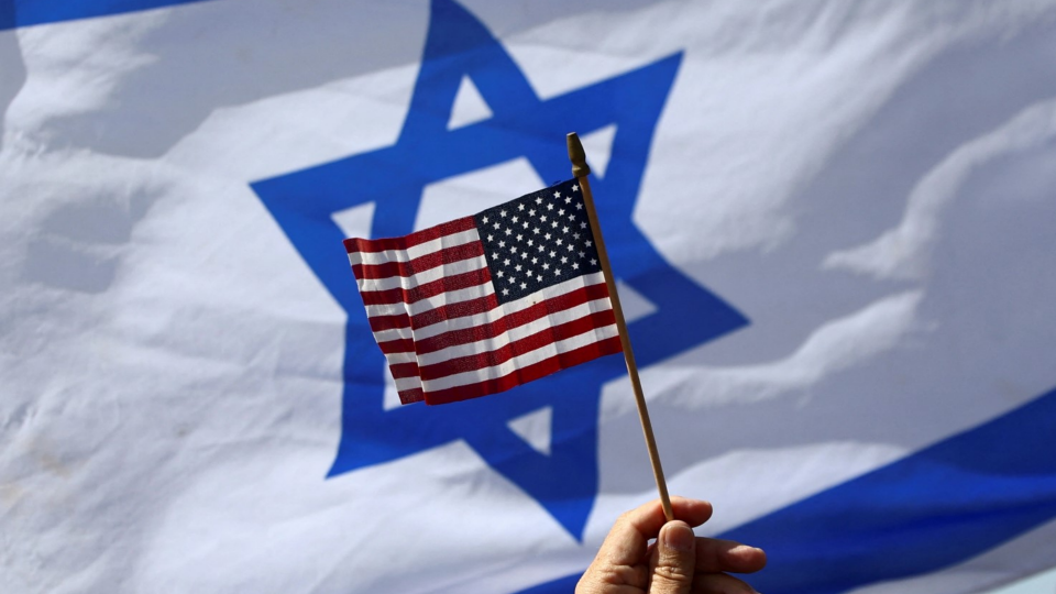 Person waves American flag with Israeli flag displayed in the background