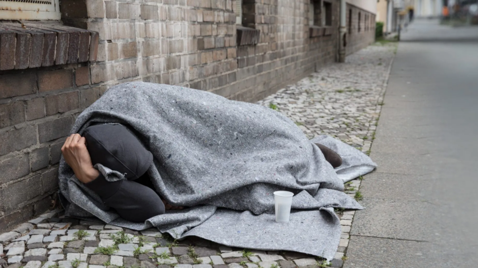 Person wrapped in a blanket laying down in the side of a street