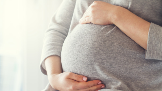 Pregnant person sitting with their hands around their torso