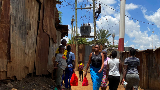 Residents walk through a walkway as a man connects electricity above the power transformer in a village in Nairobi