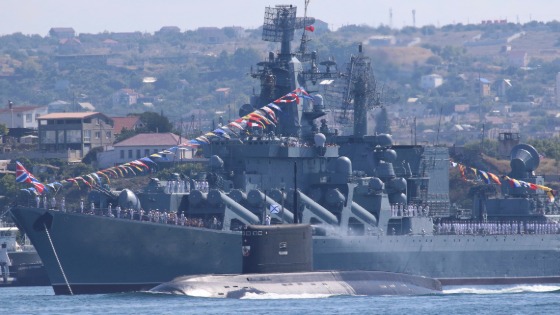 Russian sailors line up onboard a warship near a military submarine during a rehearsal for the Navy Day parade