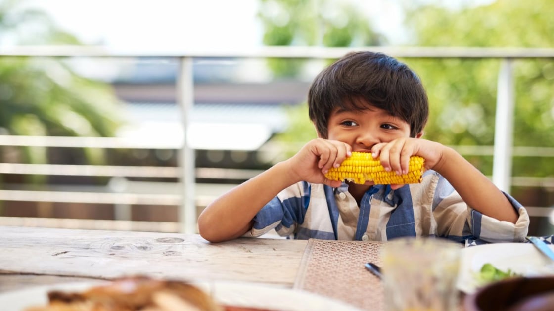 Shot of boy eating a cob of corn around a table outdoors