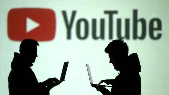 Silhouettes of mobile device users are seen next to a screen projection of YouTube logo